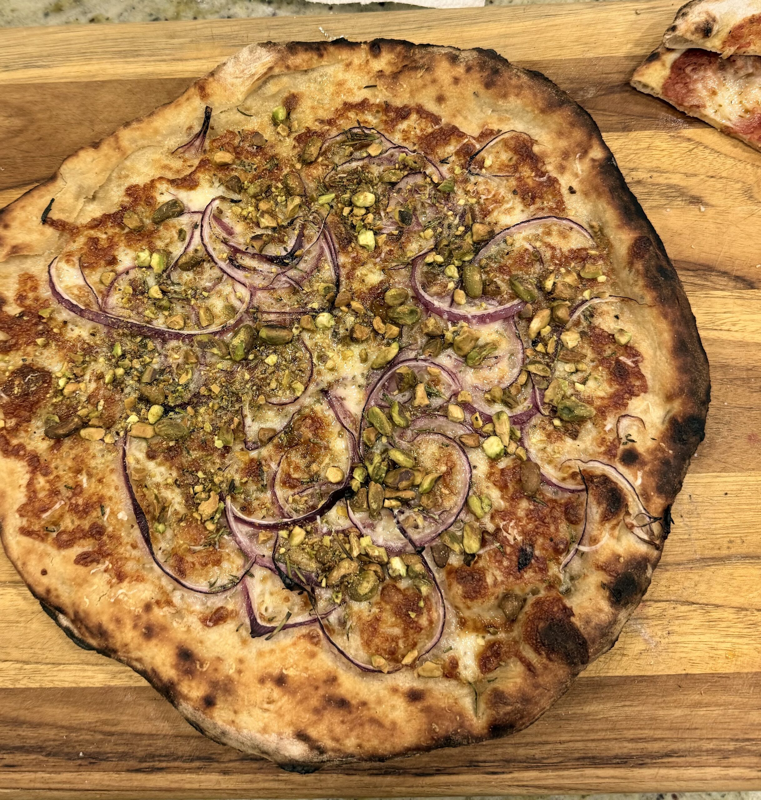 Classic rosa pizza with pistachio, red onion, and rosemary on a wooden board