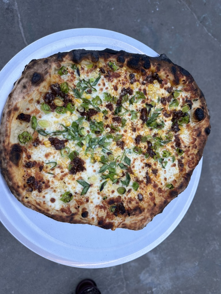 Corn, chorizo, and scallion pizza with roasted garlic cream on a white plate