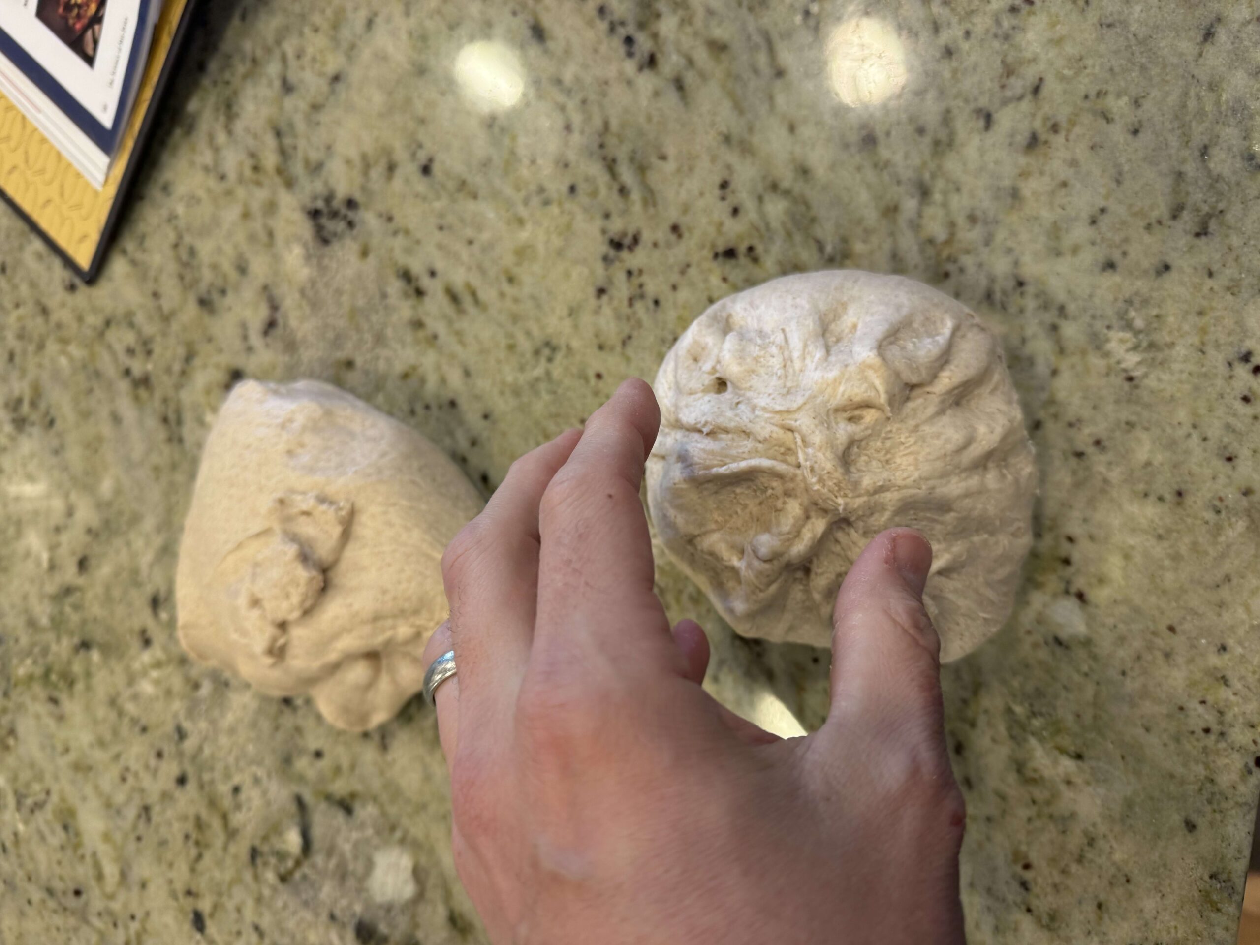Two dough balls on a countertop, one being held to show the surface