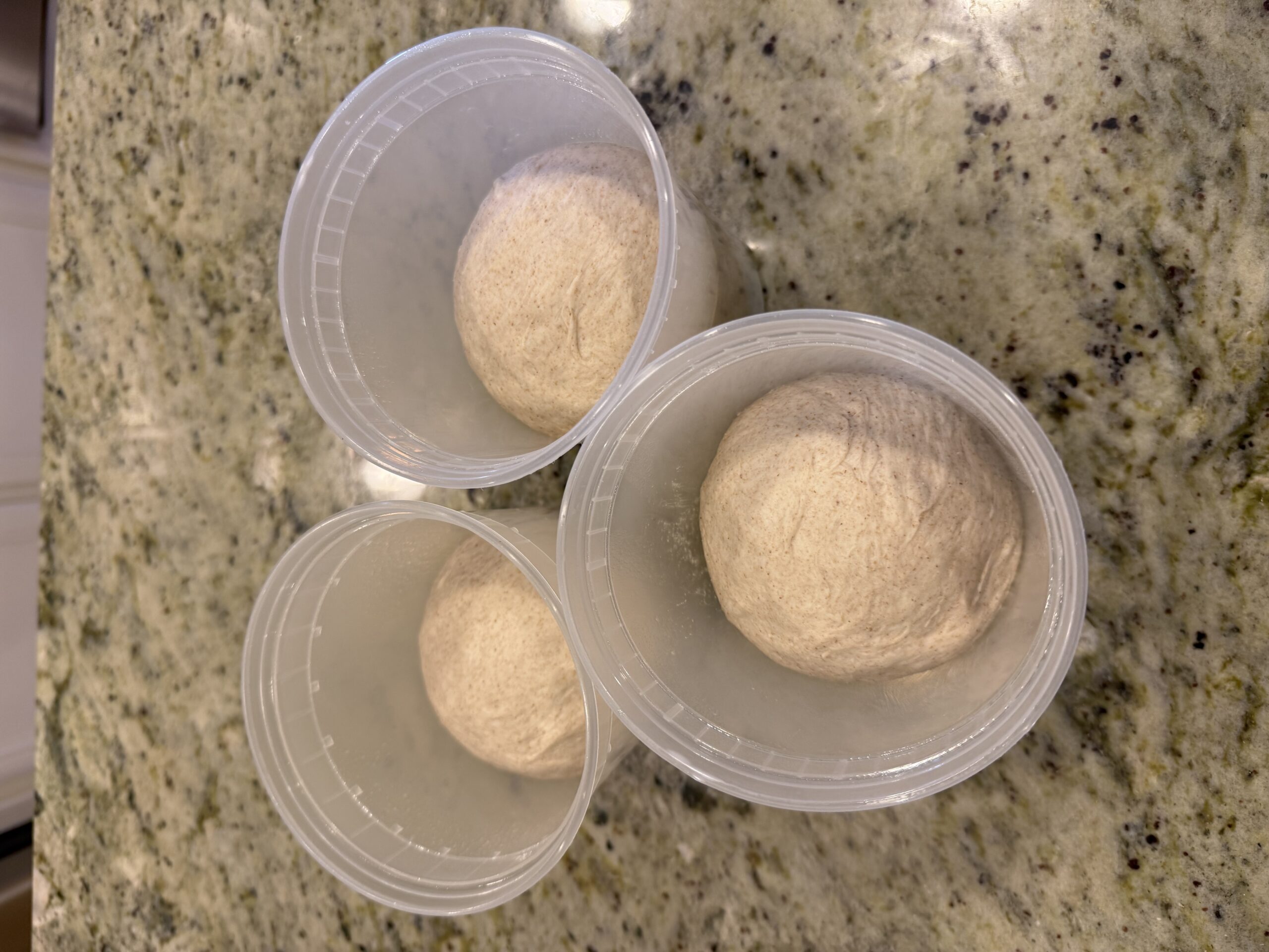 Three portioned dough balls in lightly oiled clear deli containers