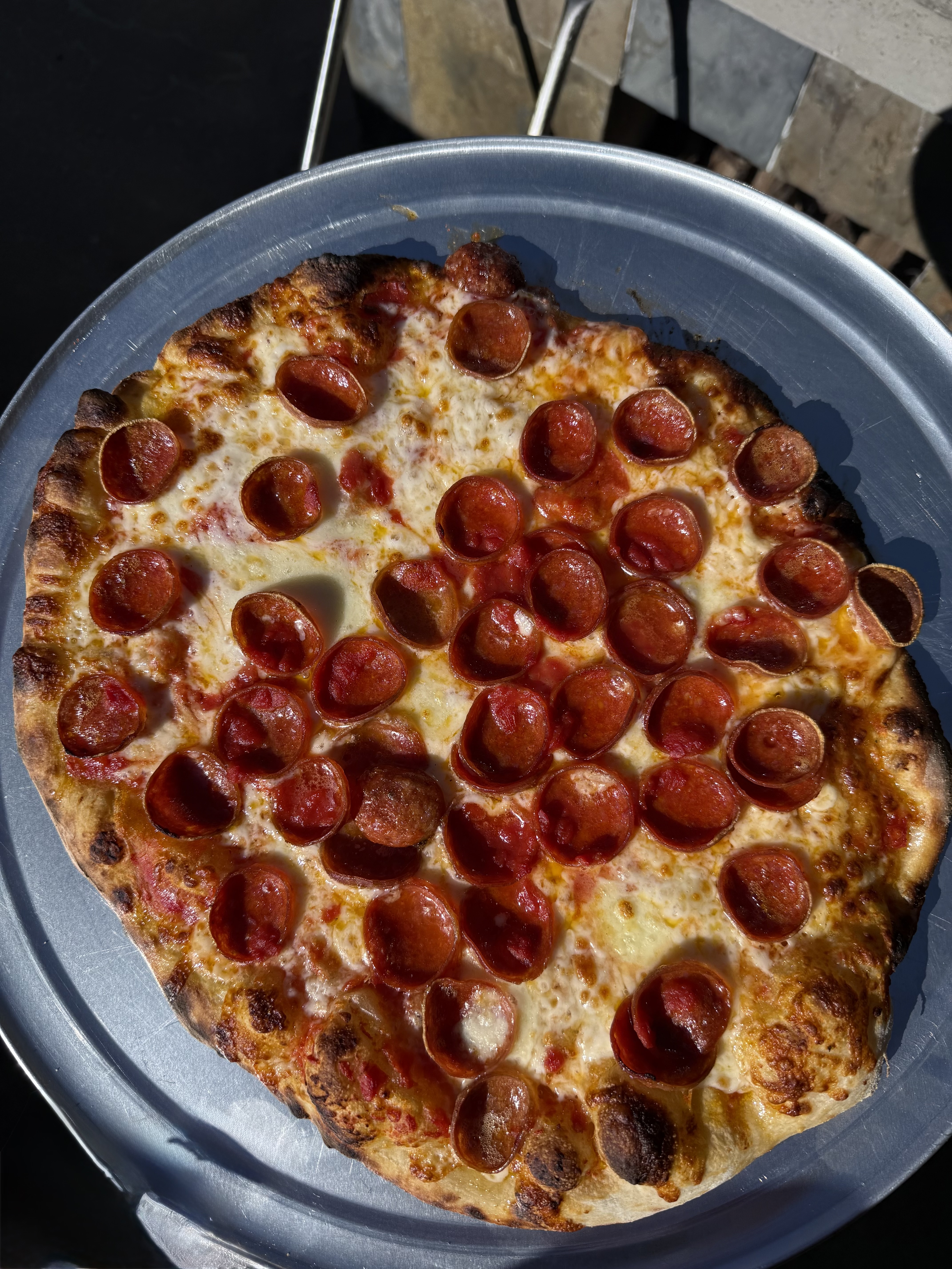 New Haven–style pepperoni pizza in a round aluminum pan, showing the thin crust and cupped pepperoni