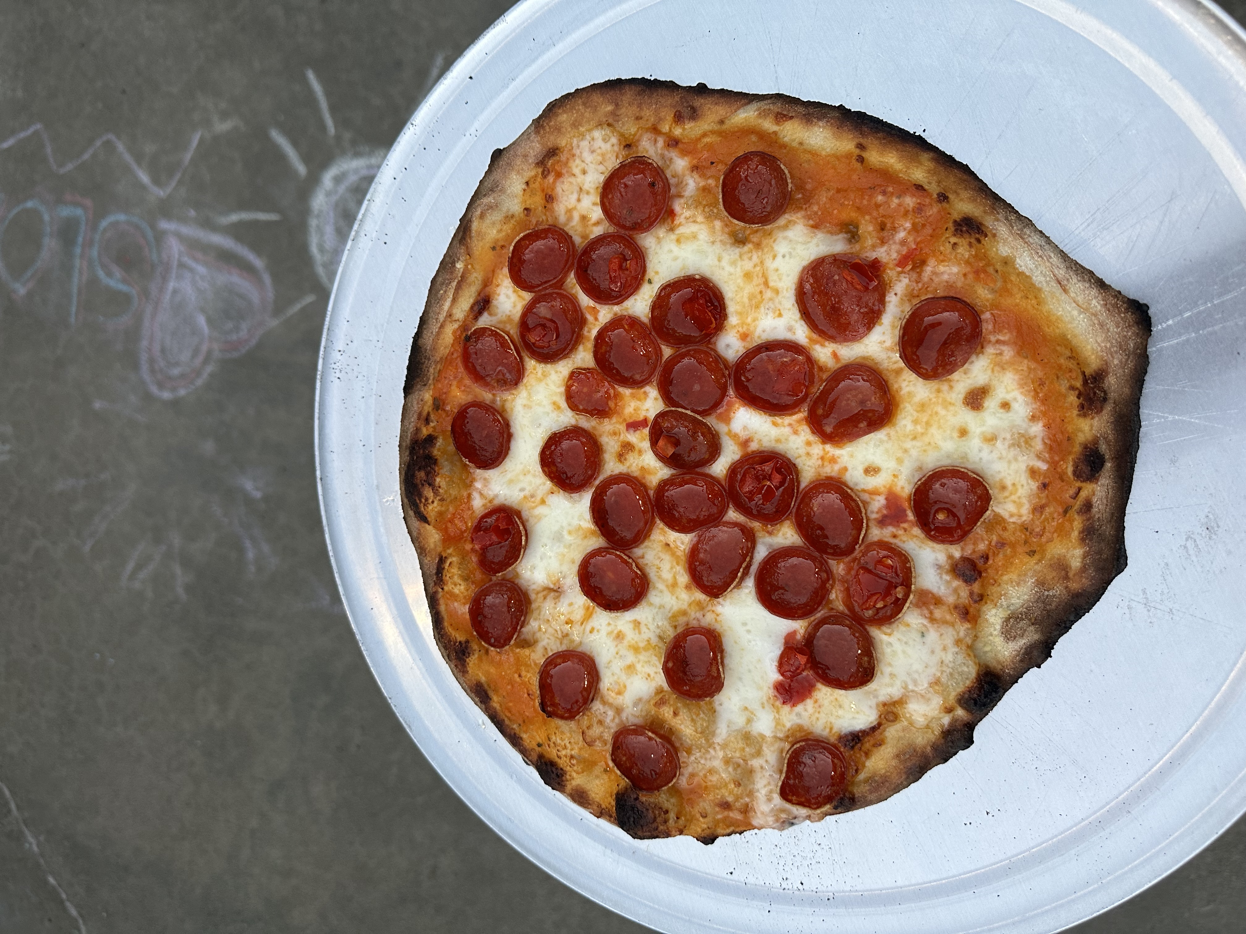 Overhead view of a deeply charred New Haven–style pepperoni pizza on a chalk-dusted surface
