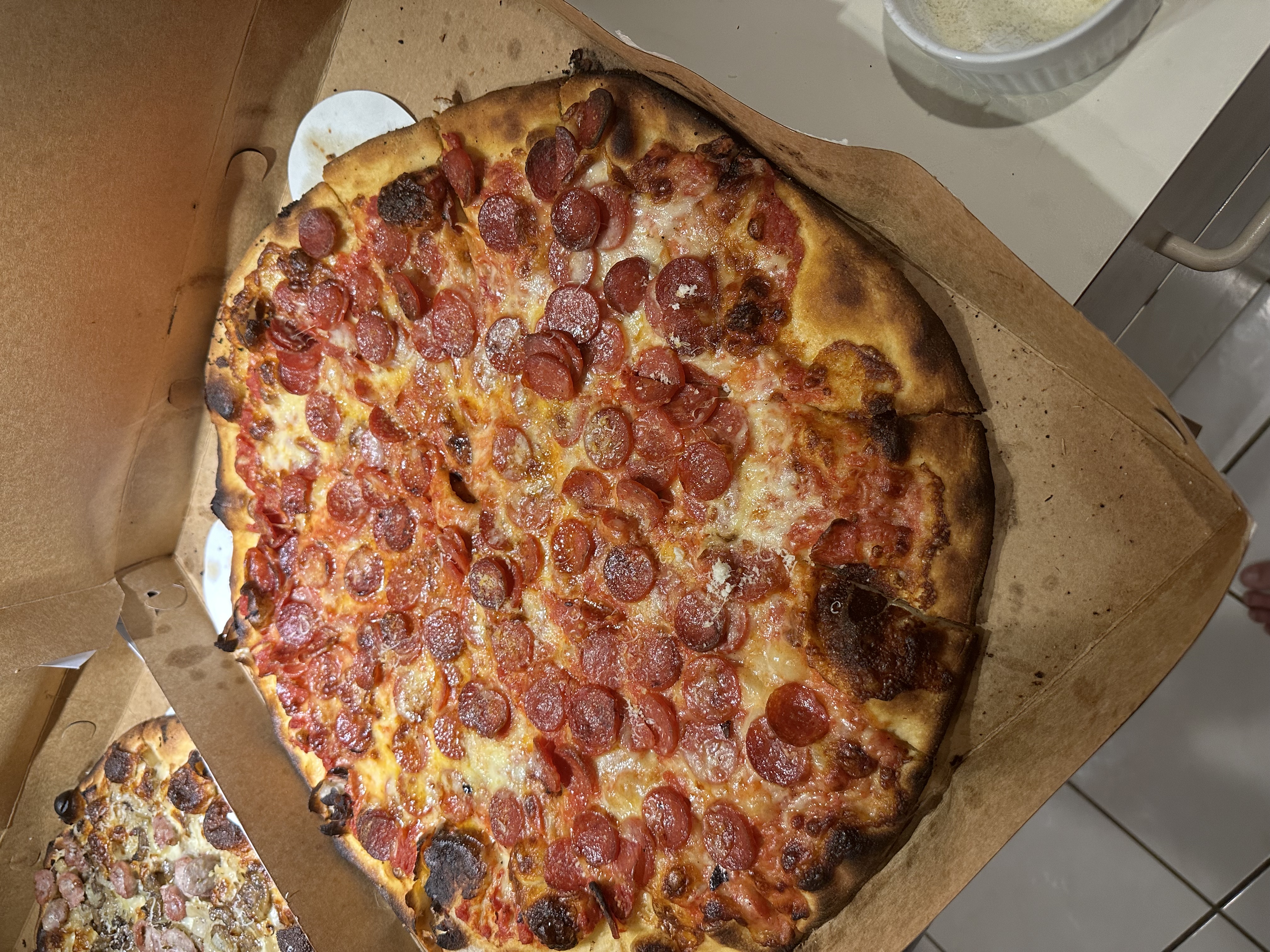 Pepperoni apizza from Frank Pepe's in a cardboard box, showing the thin charred crust and irregular shape
